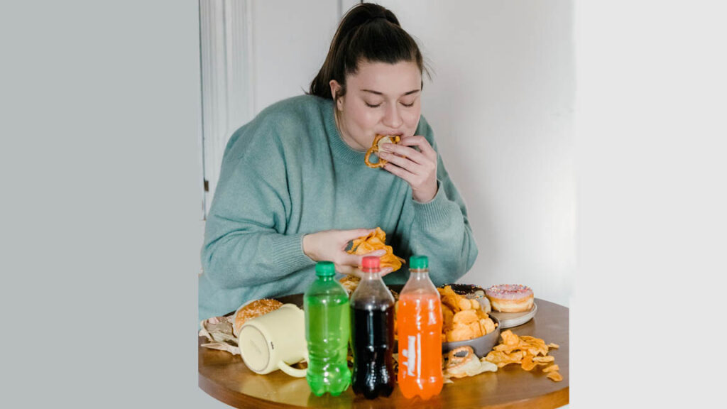 Woman eating junk food and sugary drinks contributing to obesity health risks.