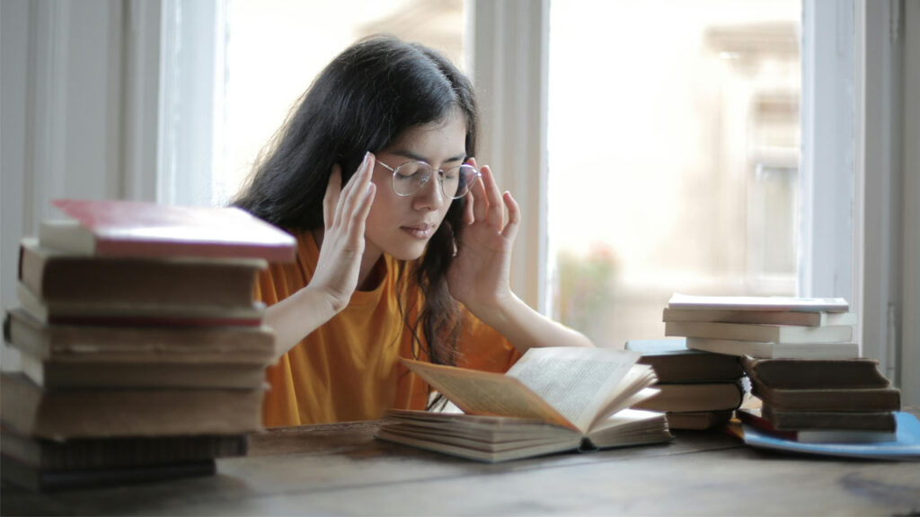 A student stressed while waiting for the WBJEE result 2025, surrounded by books.