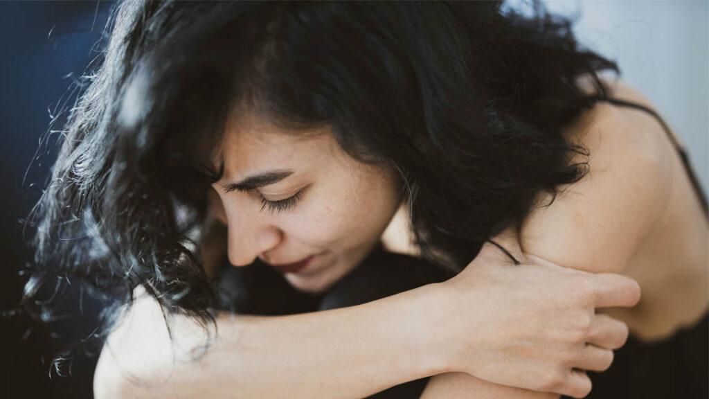 A woman holding her knees and looking down, experiencing anxiety.