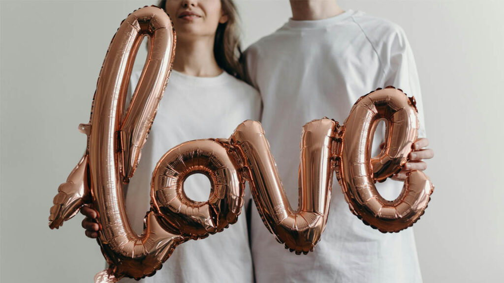 Couple holding metallic balloon letters forming the word love, symbolizing you are in love.